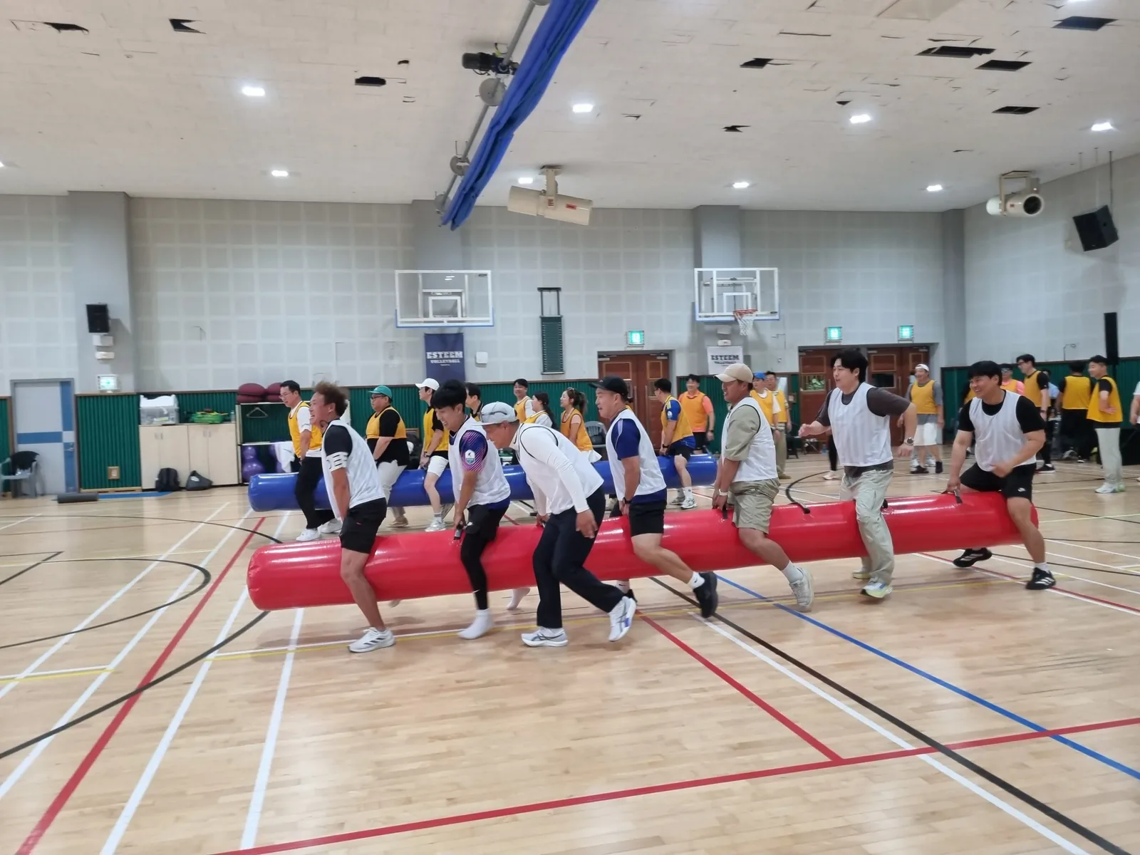 실내 체육관에서 팀별로 이어달리기 게임을 하는 참가자들